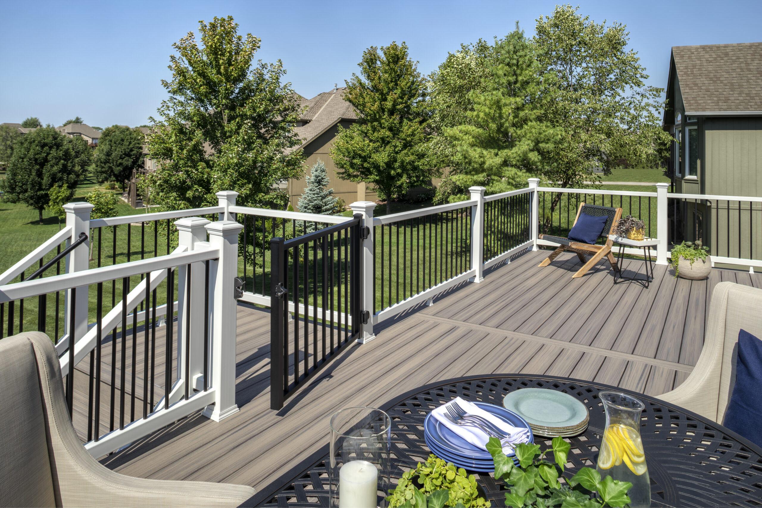 Spacious backyard deck with gray deck boards, white railing, and black balusters overlooking a landscaped yard. This outdoor living space highlights composite vs PVC decking options designed for durability, low maintenance, and long-term performance in residential settings.