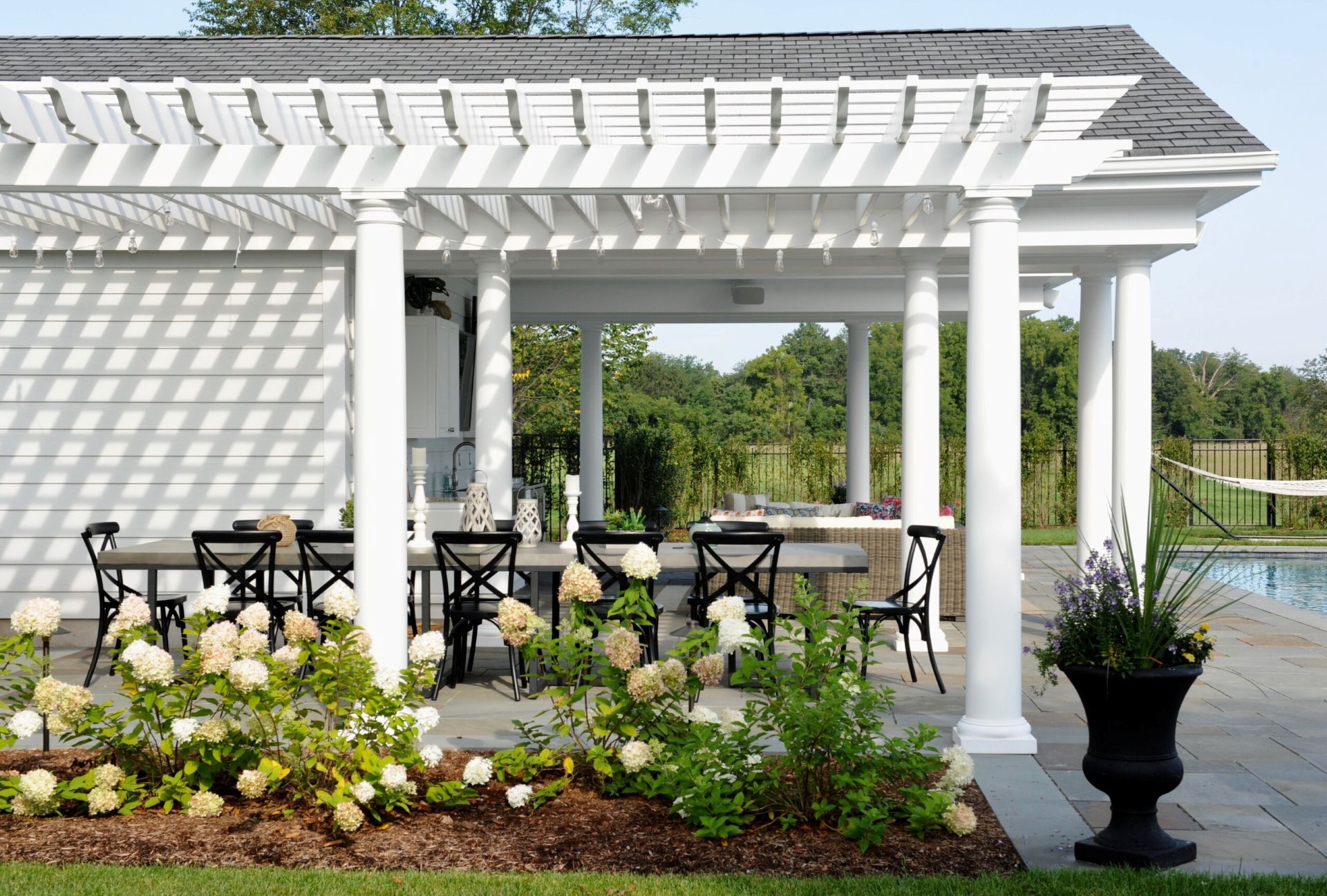 Traditional white pergola with round columns and open rafters over a patio dining area beside a pool.