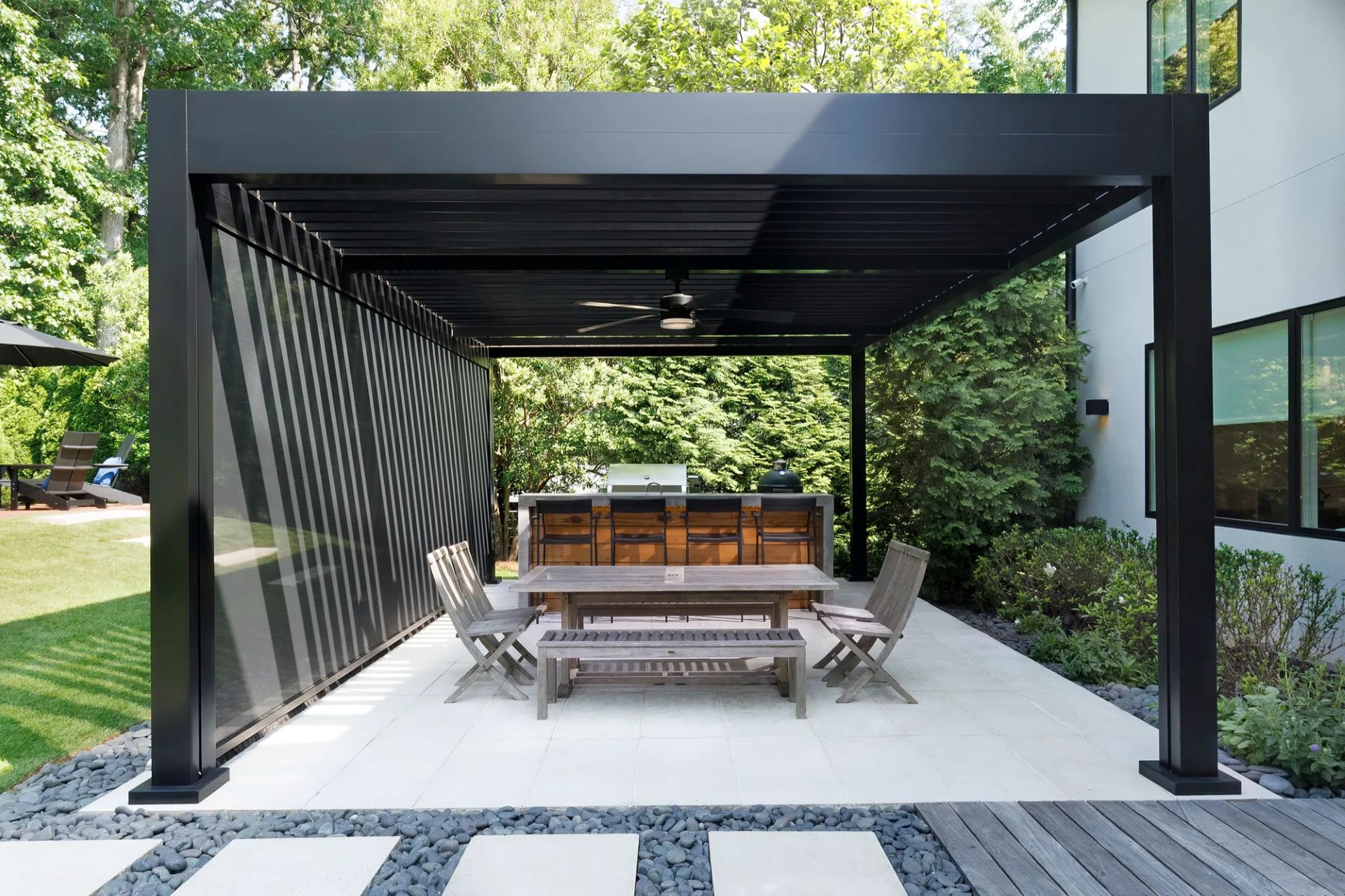 Modern black louvered pergola with side privacy screens, ceiling fan, and outdoor dining area.