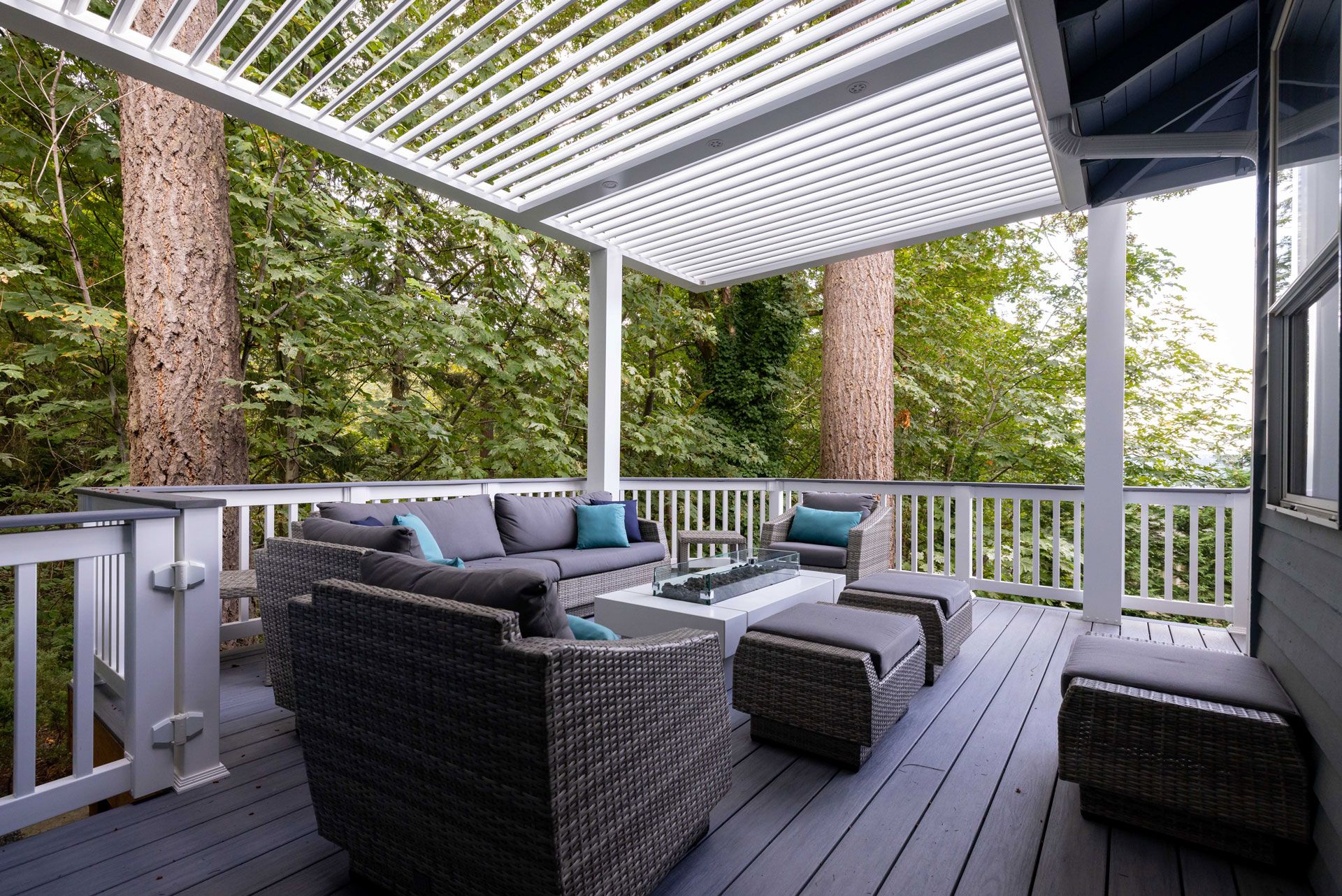 White louvered pergola over a gray composite deck with white railing and wicker lounge furniture.