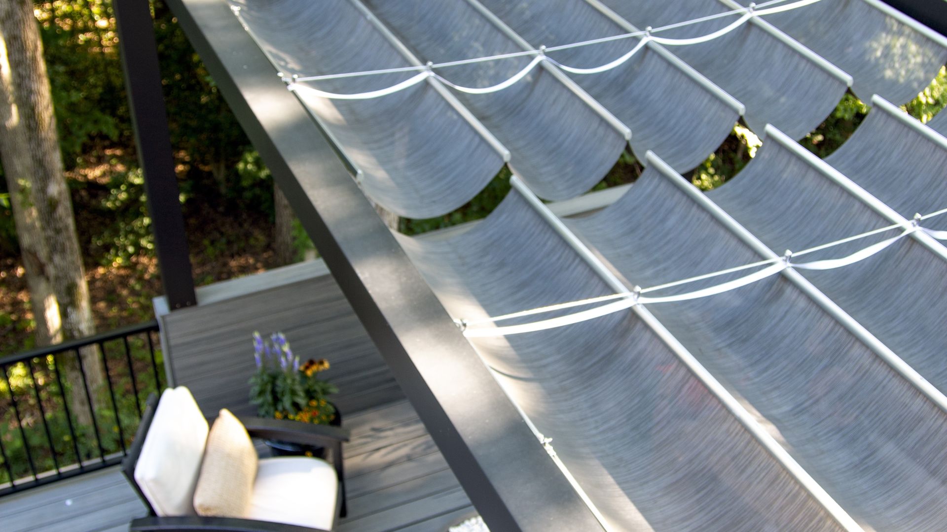 Close-up of gray fabric shade canopy panels installed on a dark metal pergola above a deck.