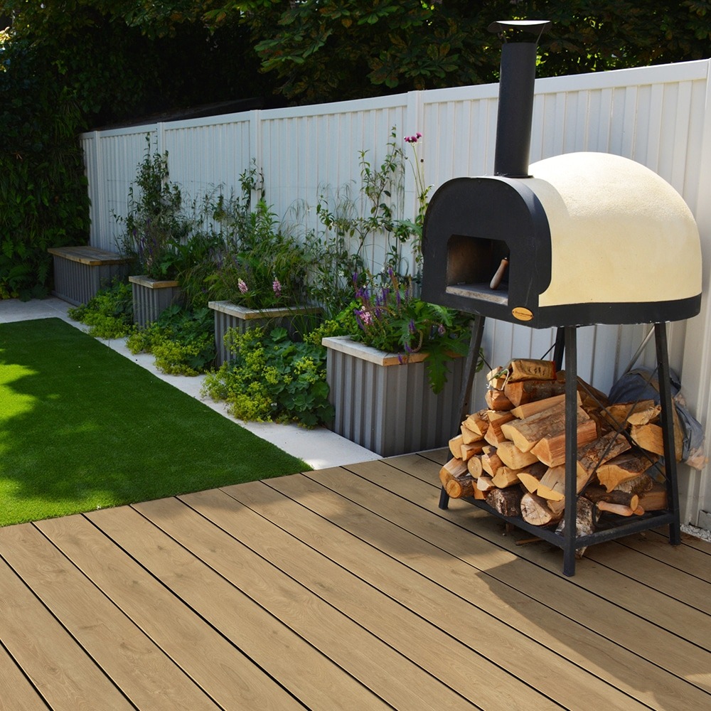 Backyard space with pizza oven and stacked firewood on Eva-Last Pioneer decking in Barrel Oak, featuring rich tan hues and natural wood detailing that enhance the cozy, rustic atmosphere.