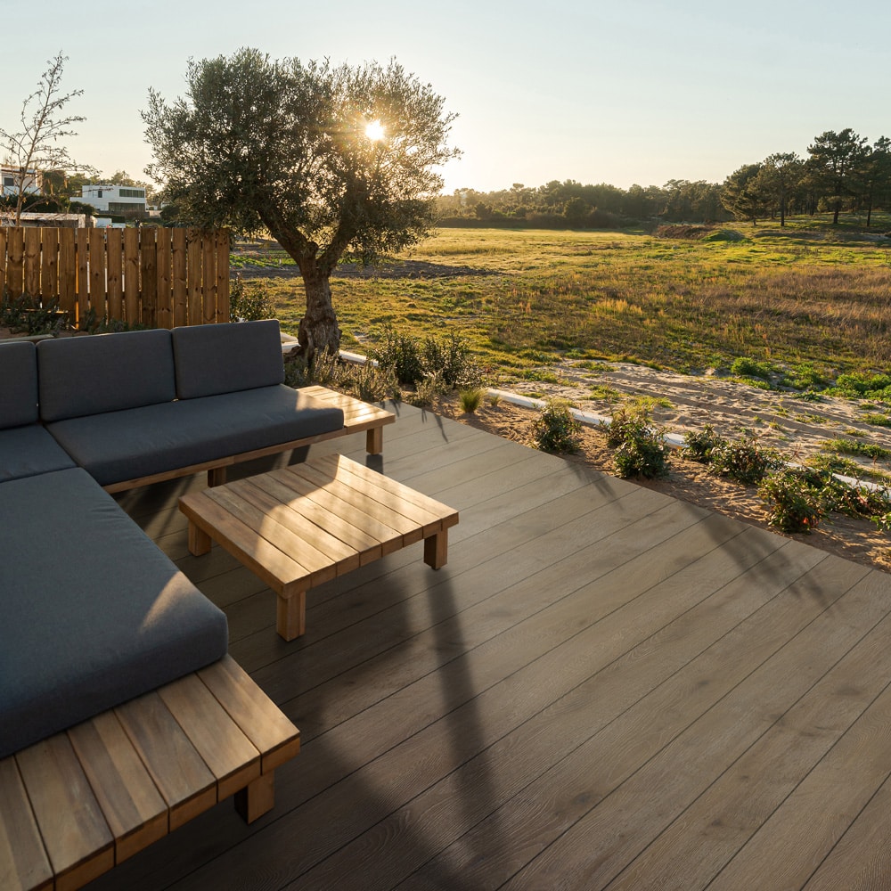 Natural Ipe boards from the Eva-Last Pioneer collection add warm contrast to an open outdoor lounge area, highlighting their low-gloss finish and natural hardwood tones under the soft evening light.