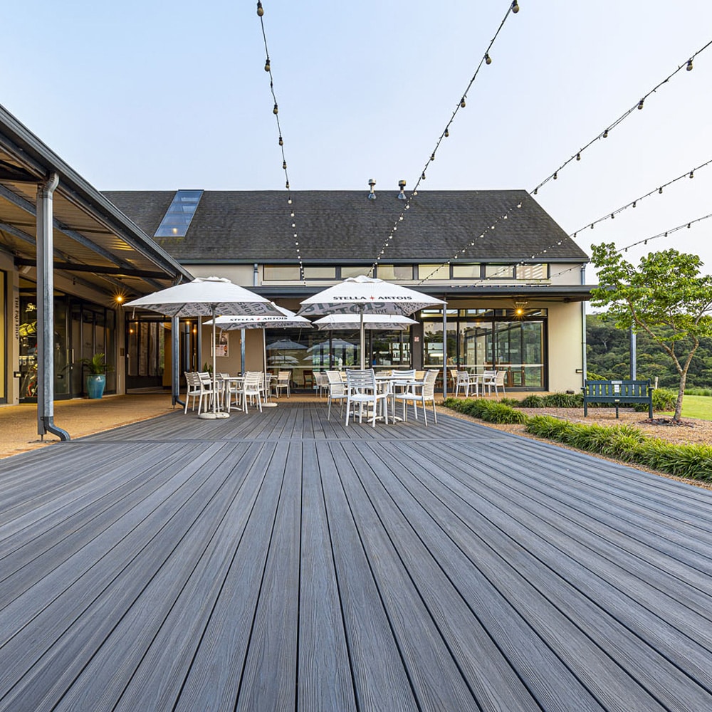 Contemporary commercial outdoor space showcasing Eva-Last Infinity IS Concrete Grey decking, set under patio lights with café-style seating.