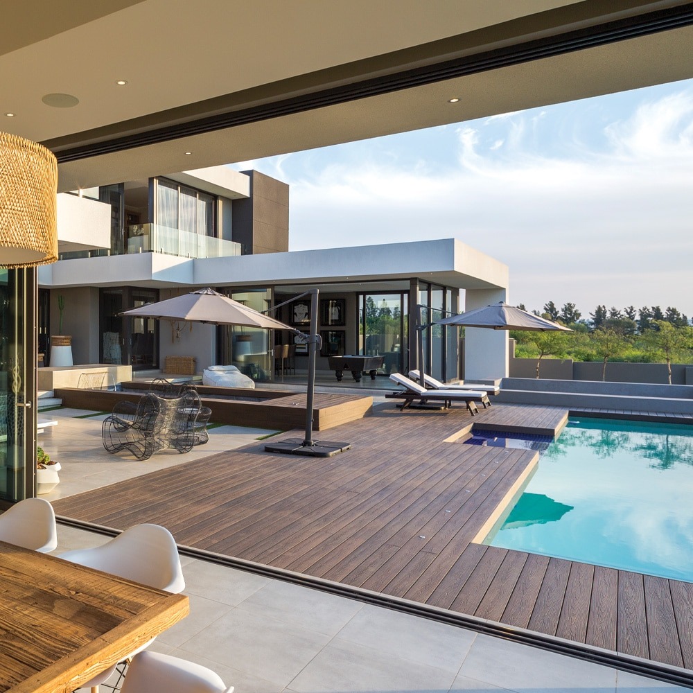 Eva-Last Infinity IS Tiger Cove decking installed around a luxury poolside patio with lounge chairs and umbrellas, showcasing its deep brown tone and matte finish.