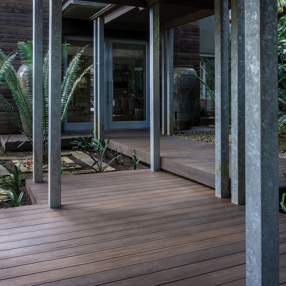 Eva-Last Infinity IS Tiger Cove decking used in a shaded entryway surrounded by greenery, highlighting the board’s earthy tone and slip-resistant surface.