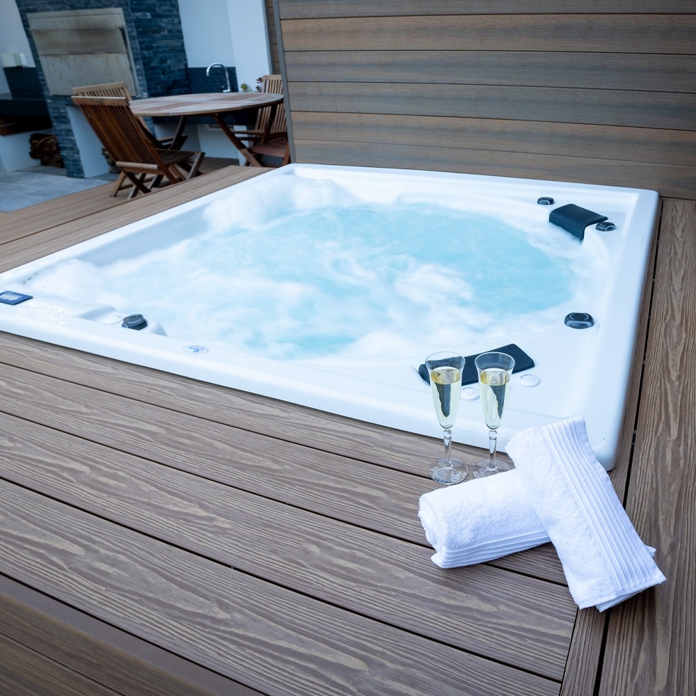 Eva-Last Eva-Tech IS Dual Tone Rusteak decking surrounding a modern white jacuzzi, styled with rolled towels and champagne flutes on the deck.