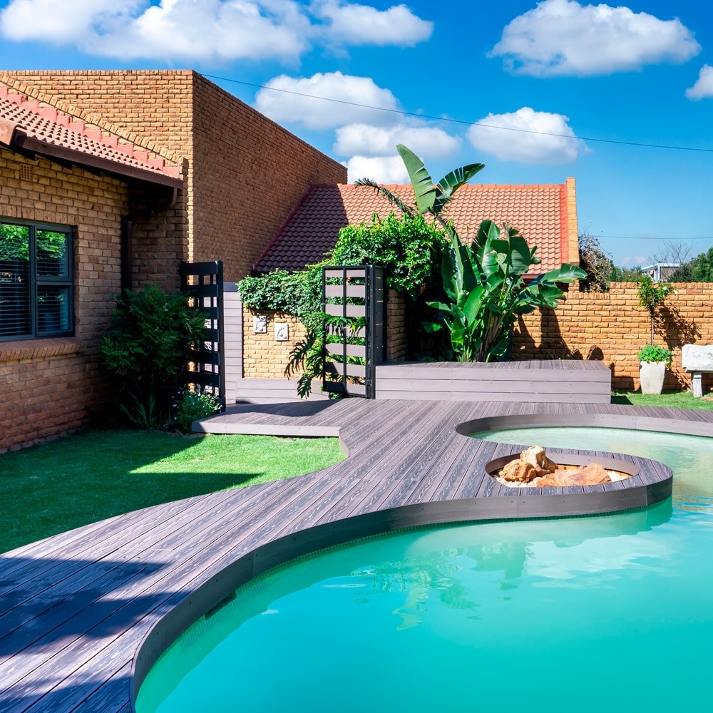 Expansive backyard pool deck made with Eva-Last Eva-Tech IS Dual Tone Rusteak boards, curved layout leading to a spa area, surrounded by brick homes and landscaping.
