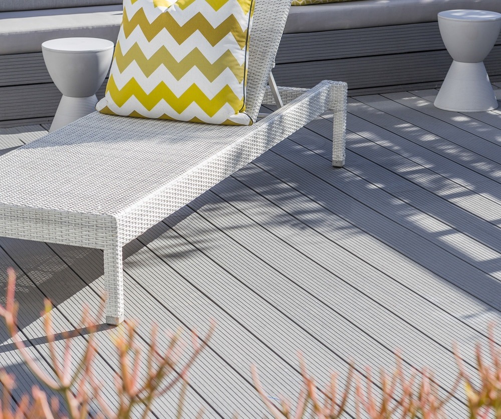 Eva-Tech IS WYDE decking in Xavia under a white lounge chair and modern outdoor furnishings, styled with bright yellow and white cushions.