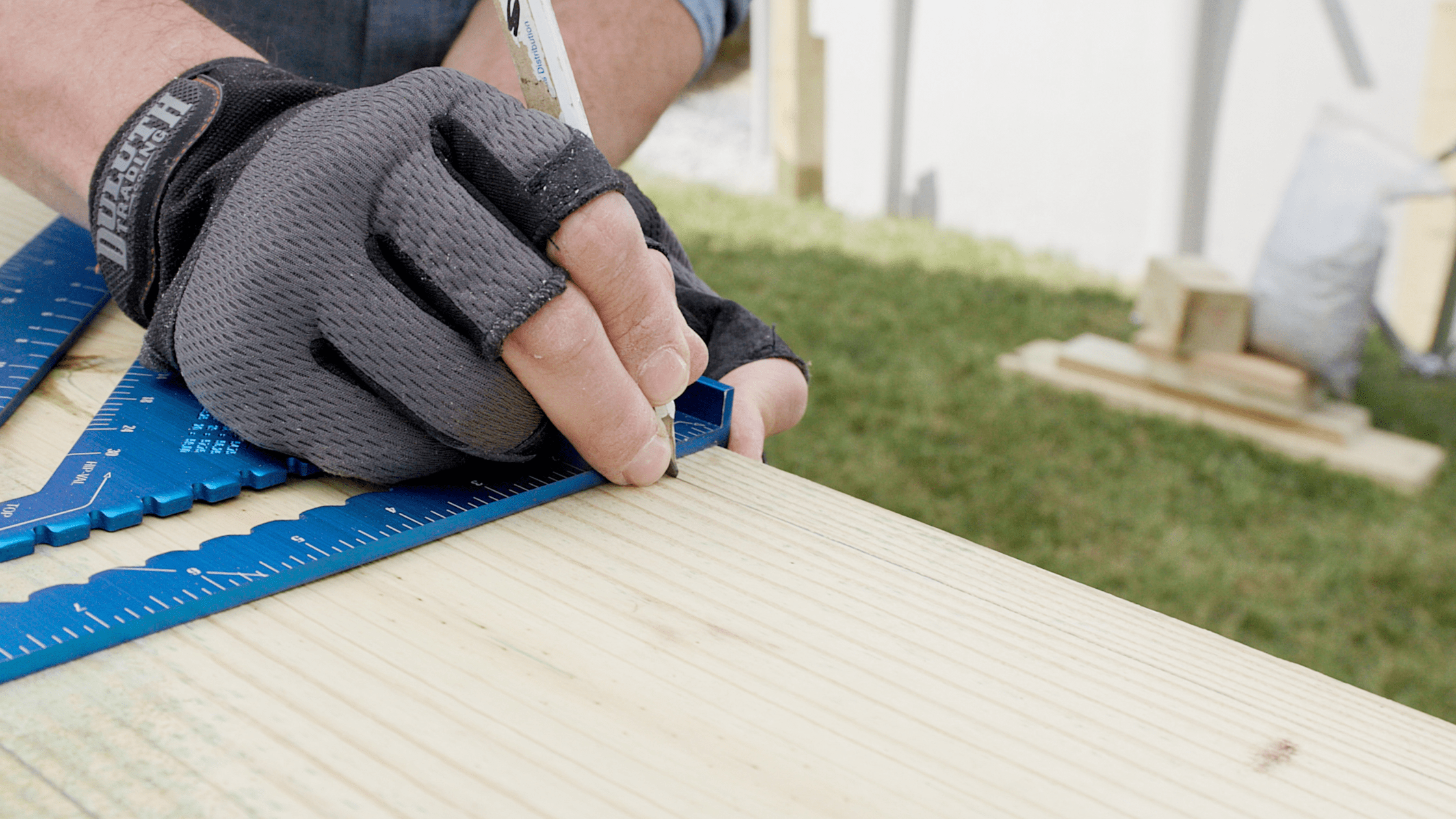 Gloved hand marking pressure-treated decking with a square, illustrating average price for a 12x12 deck replacement.