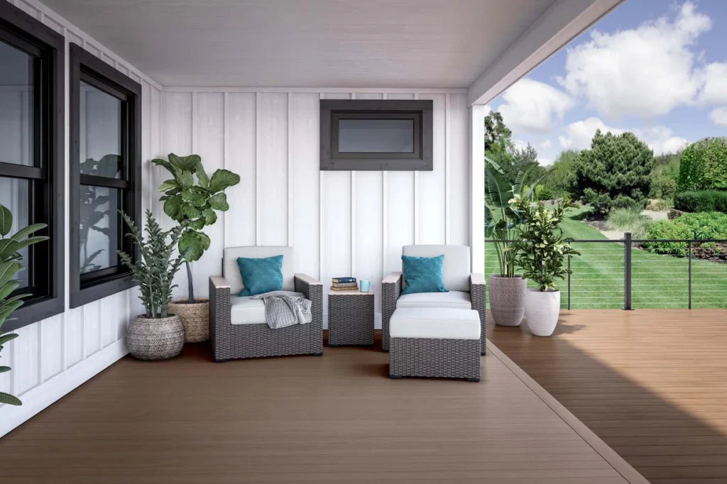 Covered front porch featuring Deckorators Porch Flooring in Chicory, paired with white siding, black trim windows, wicker patio furniture, and vibrant green plants for a cozy and elegant outdoor living space.