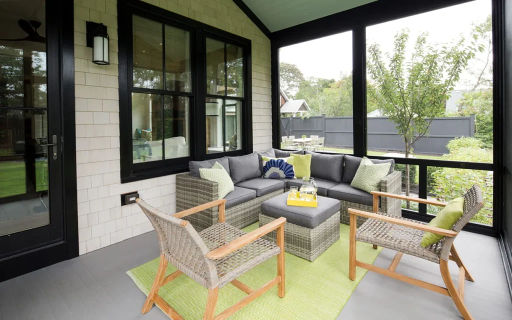 Screened-in back porch with Deckorators Kettle Gray porch flooring, wicker furniture with green and gray cushions, and black-trimmed windows providing a cozy, modern outdoor living space.