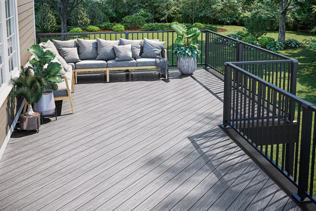 Backyard deck built with Deckorators Vault Dusk boards, styled with gray outdoor furniture and black metal railings surrounded by greenery.