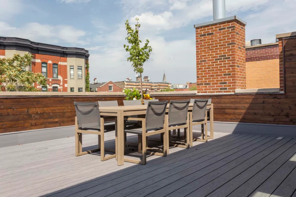 Urban rooftop dining area with long table and chairs placed over Deckorators Vault Dusk decking, framed by brick and cedar walls.