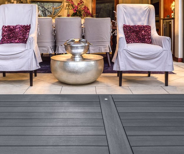 Light grey composite decking with a smooth, matte finish, shown in an upscale setting with modern silver decor and upholstered seating.