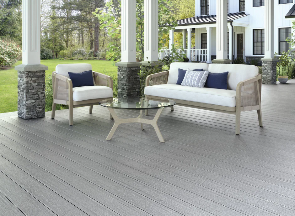 Modern covered porch featuring Fiberon Promenade decking in Moonlit Cove, with soft gray boards creating a sleek contrast against white pillars, stone bases, and neutral patio furniture.