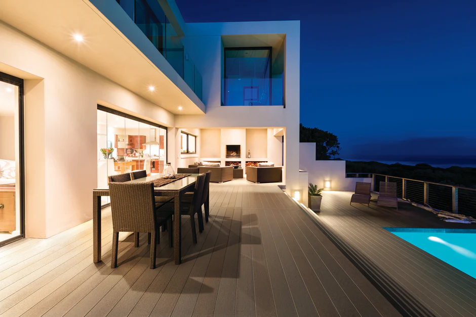 Evening view of a modern poolside patio decked in Weathered Cliff from the Promenade series, highlighted by ambient lighting, clean architectural lines, and panoramic views.