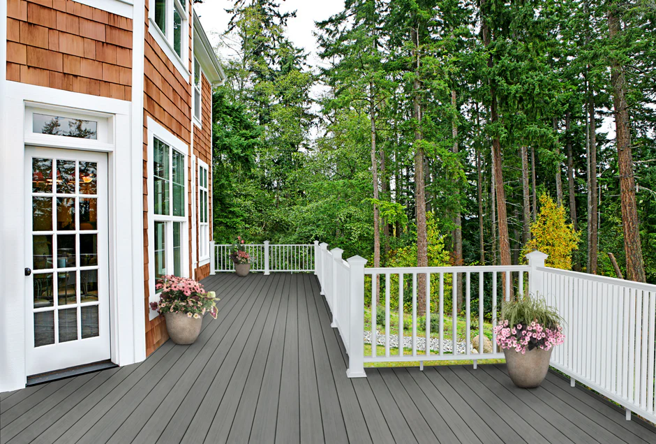 Warm grey-beige composite decking surrounded by forest views, white railings, and earthy exterior accents for a natural outdoor setting.