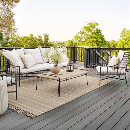 Gray composite decking with a medium grey tone, paired with woven furniture and lush landscaping in a modern, private backyard setting.