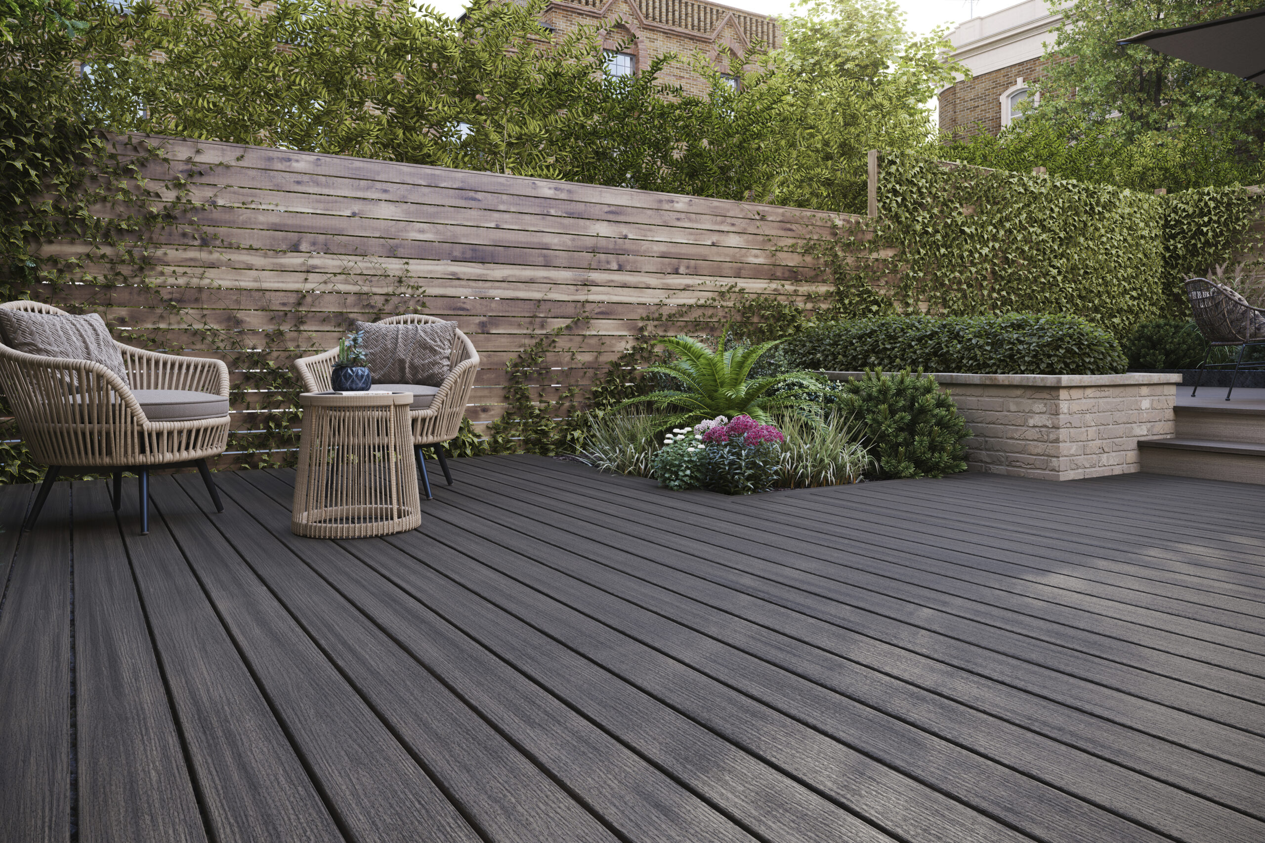 Gray composite decking with a medium grey tone, paired with woven furniture and lush landscaping in a modern, private backyard setting.