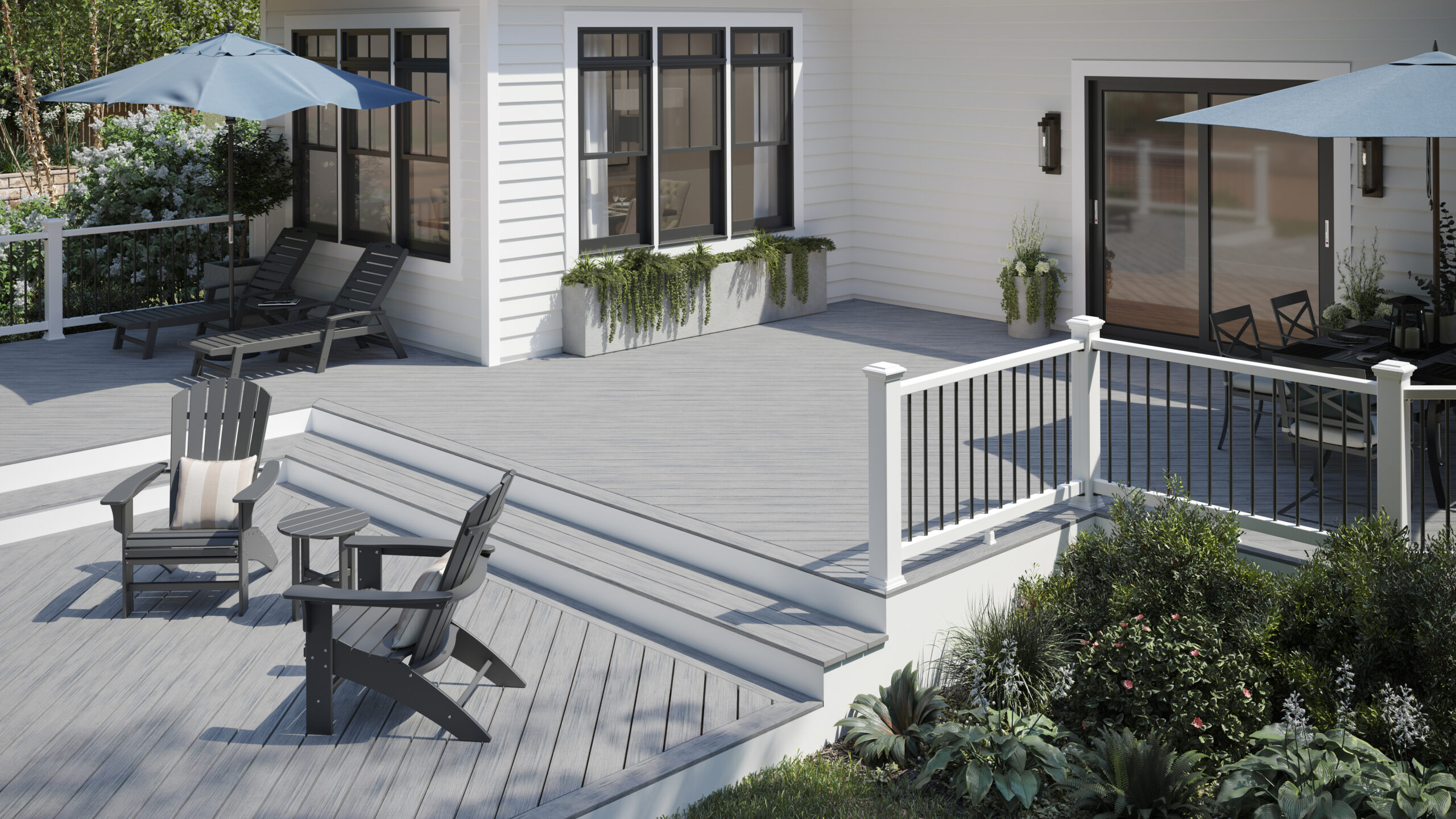 Light and medium grey composite decking styled in a bright outdoor space with white railings, black trim, and blue patio umbrellas.