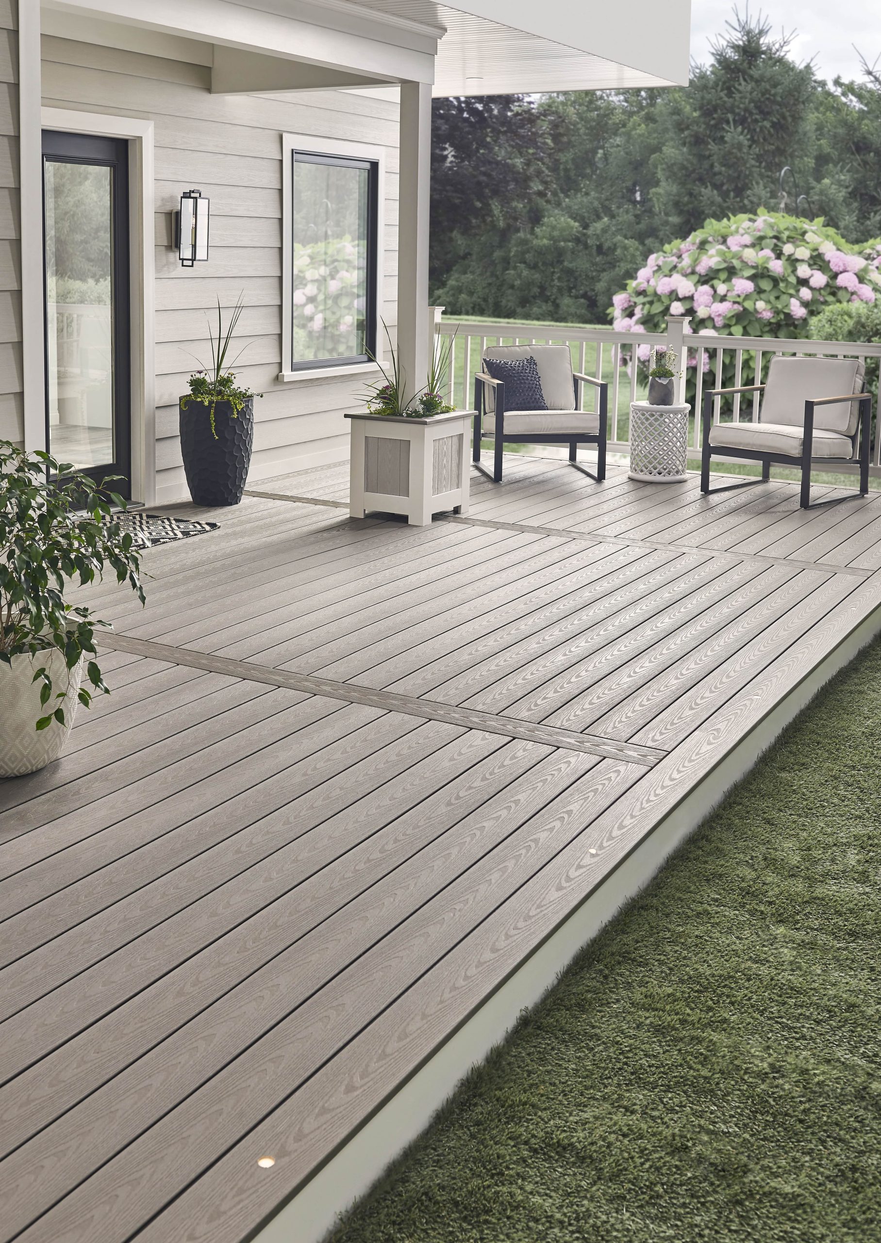 Cool grey composite decking in a bright, open porch setting with white railings, potted plants, and neutral seating accents.