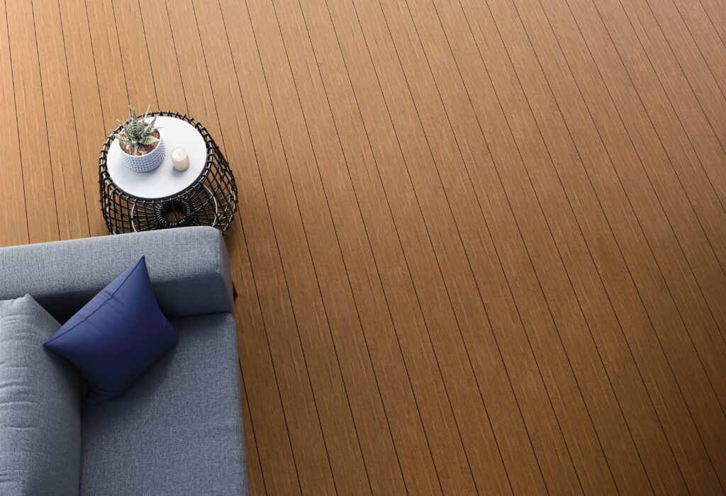 Top-down view of Fiberon Promenade Natural Reef decking with a warm wood tone, paired with a gray sofa and navy pillow, and a round table with decorative items, highlighting the smooth grain and clean installation.