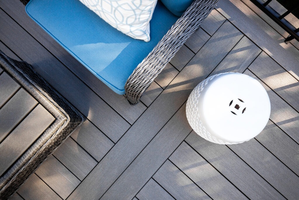 A cozy scene with a couple relaxing on a bamboo daybed placed on Fiberon Promenade Shaded Cay decking, surrounded by lush greenery and soft natural lighting that highlights the deck’s warm gray color.