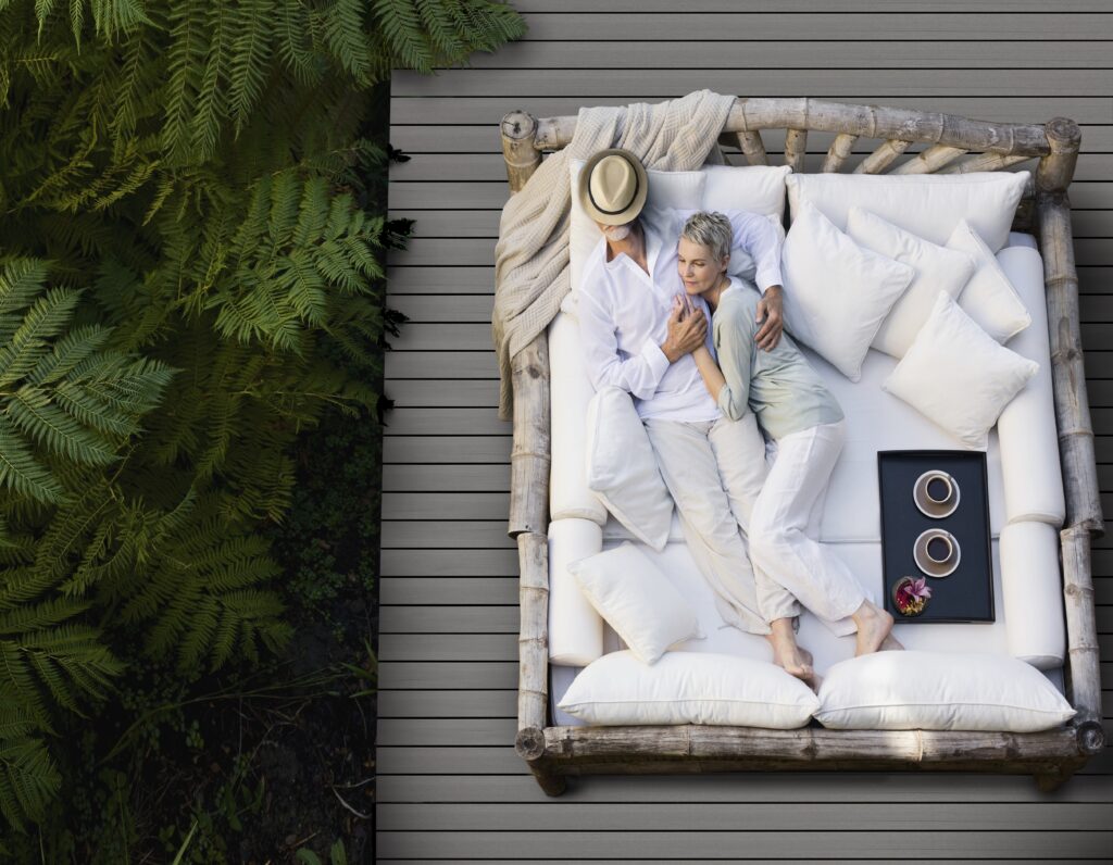 Overhead view of an outdoor deck built with Fiberon Promenade Shaded Cay decking, featuring a woven chair with blue cushion and a white ceramic garden stool, highlighting the board’s modern gray tones and clean layout.