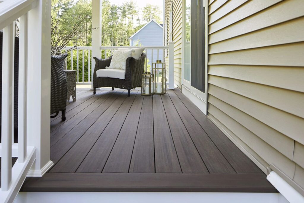 Covered front porch with TimberTech Landmark American Walnut PVC deck boards, featuring a wicker lounge chair and decorative lanterns for a cozy welcome.