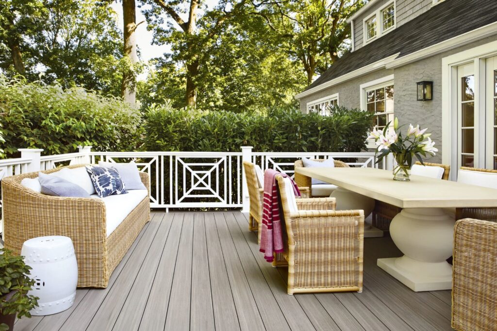 Outdoor dining area featuring TimberTech Vintage Coastline™ PVC decking with soft gray tones, surrounded by white railing and wicker furniture, creating a bright and inviting backyard setting.