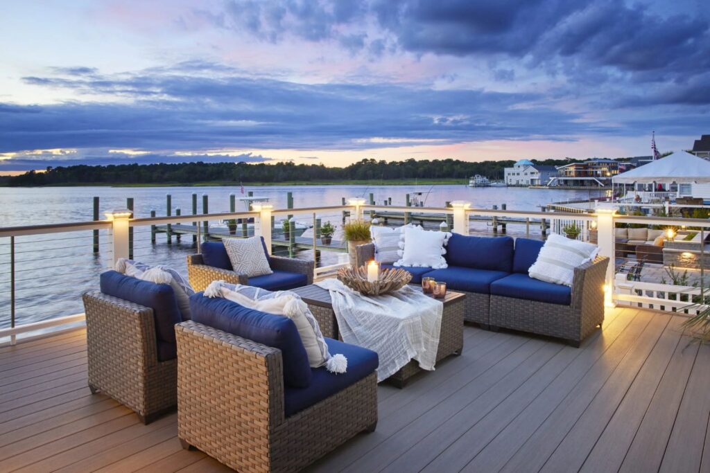 TimberTech Vintage Coastline™ deck overlooking a waterfront marina at sunset, with cozy seating and nautical-inspired decor, blending laid-back luxury with durable PVC construction.