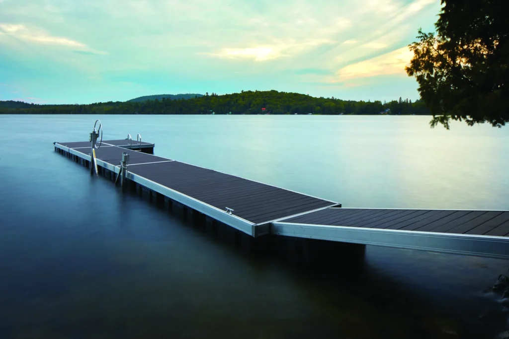 A long lakeside dock built with TimberTech Vintage Dark Hickory PVC decking, stretching over calm waters under a soft, overcast sky.