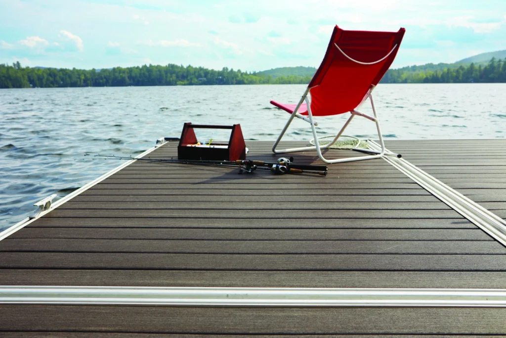 A lakeside dock featuring TimberTech Vintage Dark Hickory decking with a red chair and fishing gear set up for a peaceful day by the water.