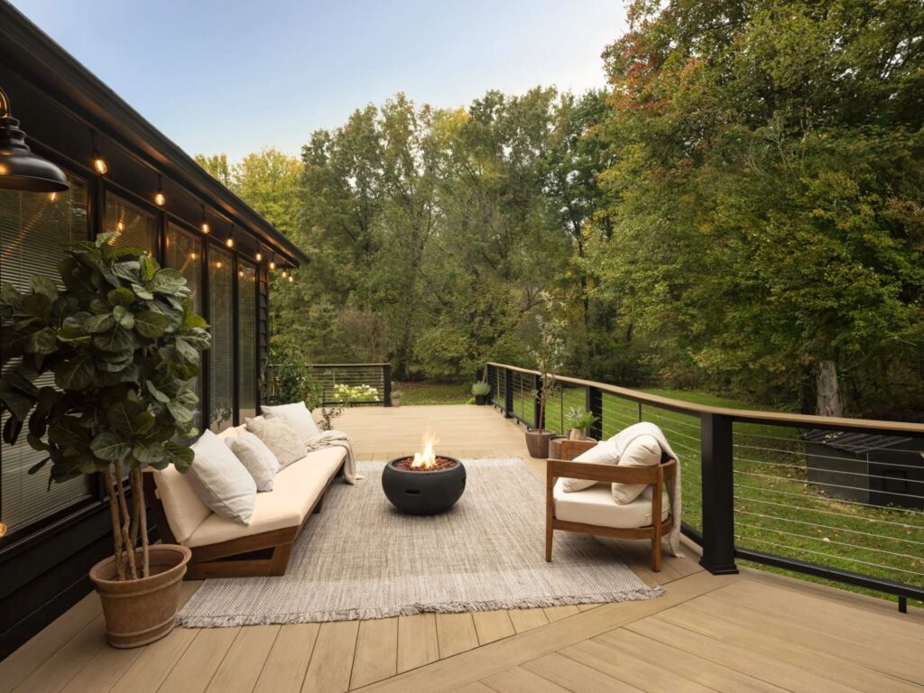 TimberTech Vintage Weathered Teak deck styled with a cozy seating area, string lights, and a black fire bowl, surrounded by a wooded backyard for a warm, inviting escape.