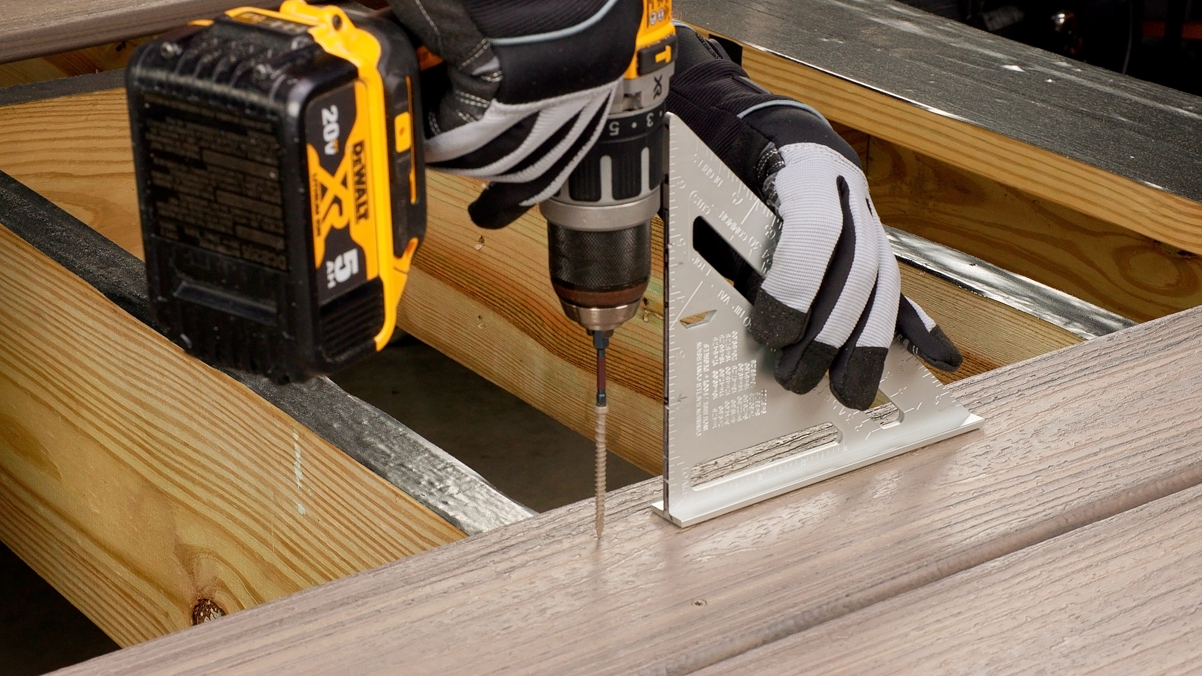 A contractor installs composite deck boards using a power drill and decking frame screws. The image shows a worker aligning the board with a square tool, ensuring proper placement. The decking frame screws provide strong structural support, securing the boards to the underlying joists for a stable and long-lasting deck. It features the best deck screws to use