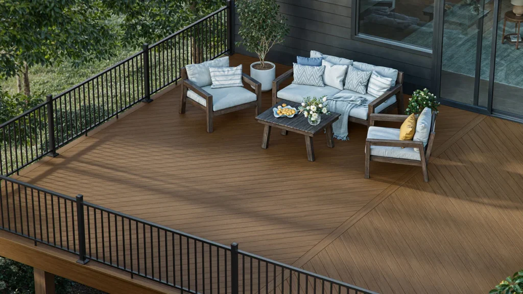 Elevated deck featuring Deckorators Summit Boulder boards with black railing and cozy outdoor furniture. The medium brown tone adds natural warmth to the space, surrounded by trees and greenery.