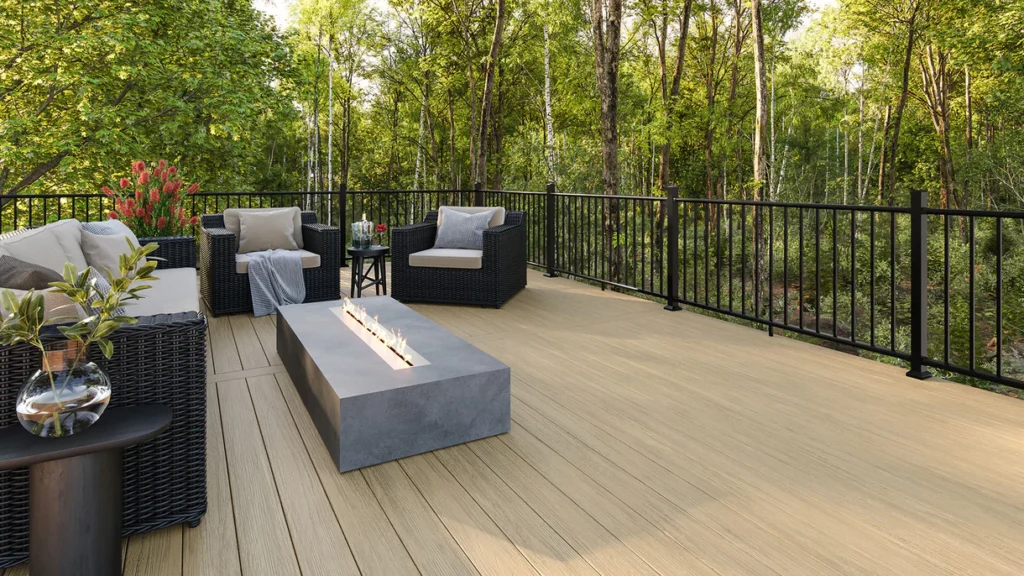Deck built with Cliffside boards overlooking a wooded landscape. The light tan decking pairs with black railings and modern black wicker furniture around a concrete fire feature.