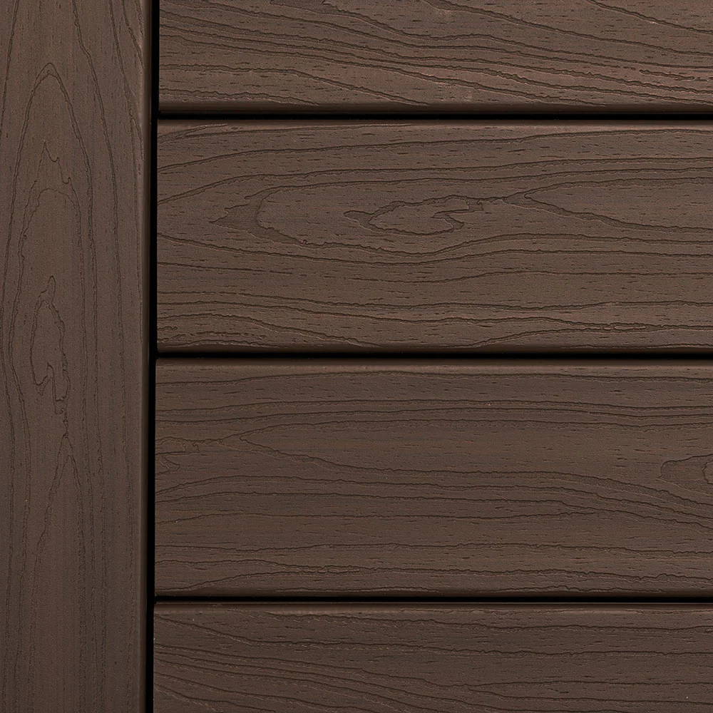 Close-up of Deckorators Tropics Decking in Hana Brown, showcasing rich brown tones with natural-looking woodgrain patterns. The surface mimics tropical hardwood with subtle texture and low-gloss finish, ideal for classic outdoor designs. Durable scalloped-edge composite boards shown in horizontal layout.