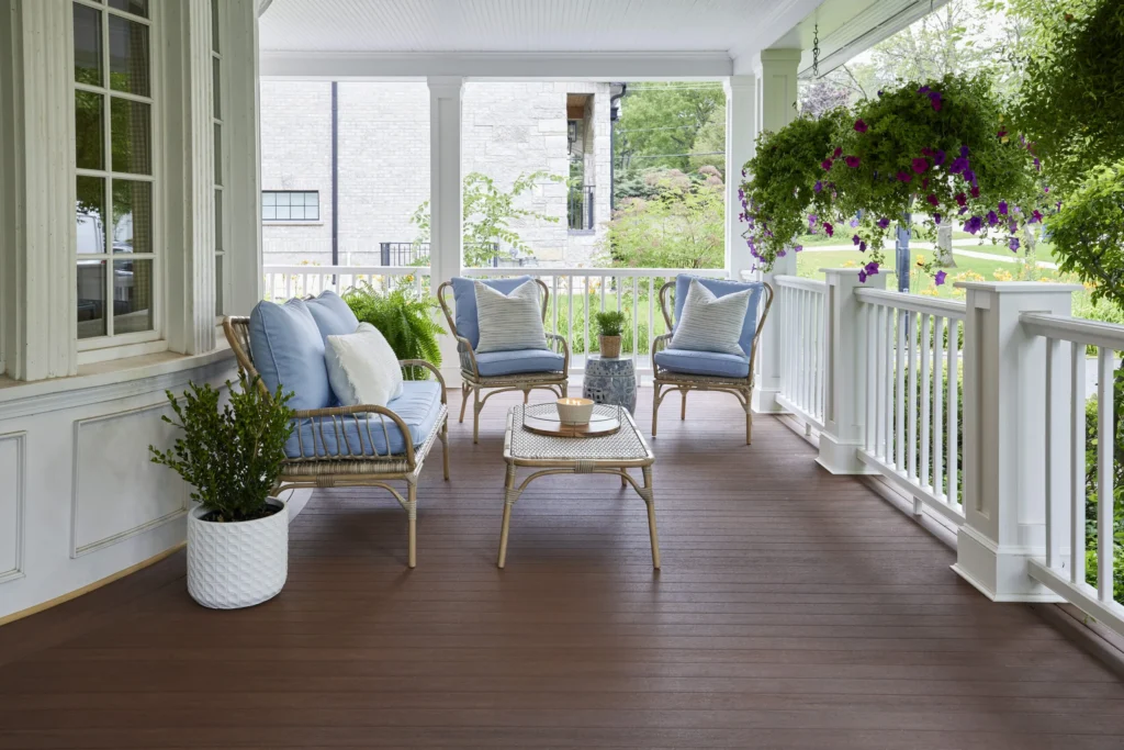 A cozy front porch outfitted with TimberTech Mahogany decking, framed by crisp white railings and adorned with wicker seating and pastel blue cushions. The deep, reddish brown floorboards bring warmth and contrast to the soft color palette of the space, creating an inviting, elegant retreat.