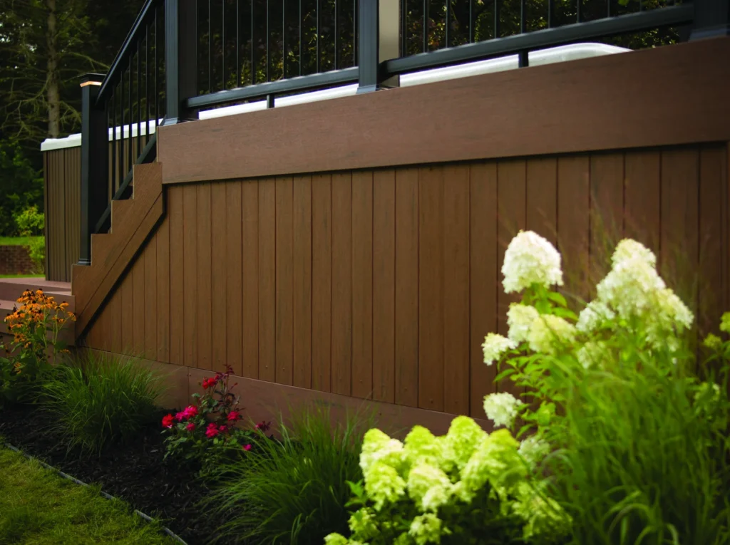 TimberTech Terrain Brown Oak composite decking shown in a raised backyard deck design with black railings and lush landscaping, highlighting its rich brown color and natural wood grain texture.