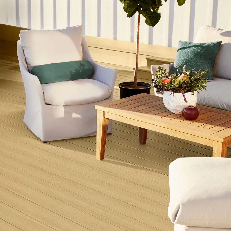 A cozy outdoor seating area featuring soft white cushions and a wooden coffee table sits atop TimberTech Terrain+™ Natural White Oak composite decking, which radiates warmth and a clean, natural look under soft daylight.