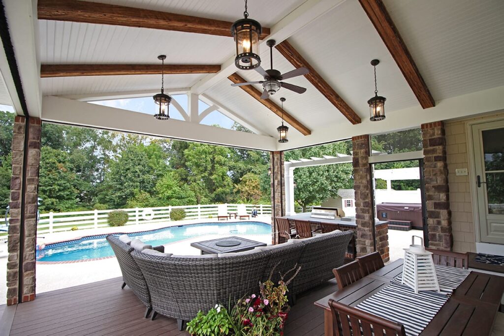 Covered poolside deck built with TimberTech Terrain Rustic Elm composite decking, showcasing its rich brown tones and cathedral grain texture beneath a white pergola and outdoor seating.