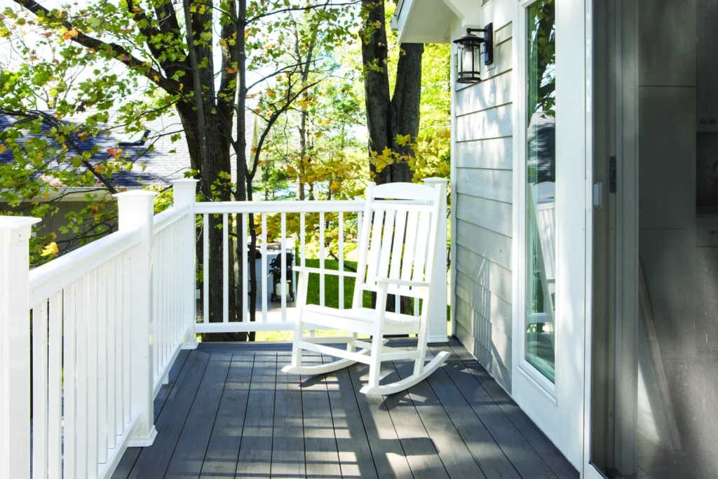 A cozy front porch deck built with TimberTech Terrain Silver Maple composite decking boards, featuring a clean white railing and a single white rocking chair overlooking a peaceful tree-filled yard.