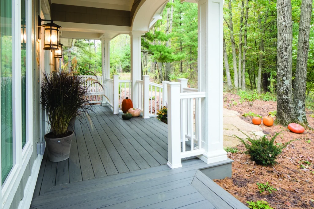 Inviting front porch made with TimberTech Terrain Silver Maple composite decking, styled with white railings, pumpkins, and seasonal plants against a backdrop of autumn trees.