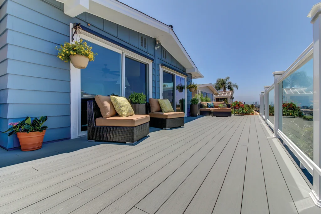Modern rooftop deck built with TimberTech Terrain Stone Ash composite decking, featuring clean glass railings, wicker furniture, and vibrant potted plants for a sleek, coastal-inspired outdoor retreat.