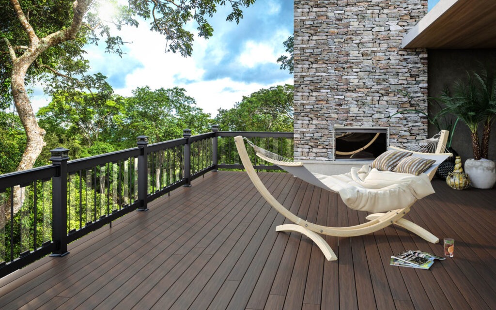 Deckorators Tropics Hana Brown decking with black aluminum railing and hammock chair on a modern outdoor deck overlooking a lush green forest.