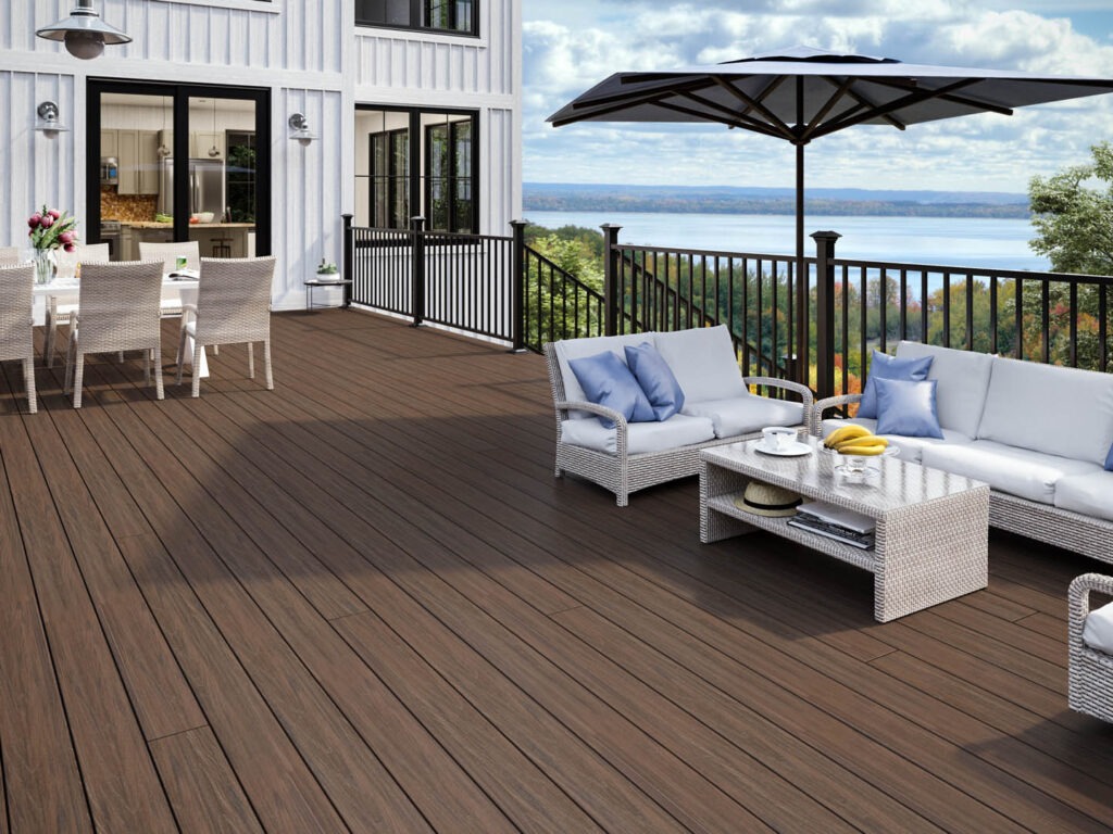 Modern lakefront deck with Deckorators Tropics Hana Brown decking and black railings, styled with white outdoor furniture and a scenic view of the water.