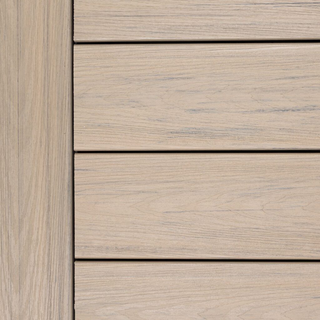 Close-up swatch of Deckorators Venture Shoreline decking showing a light sandy beige tone with soft gray woodgrain streaks and a natural, sun-washed appearance.