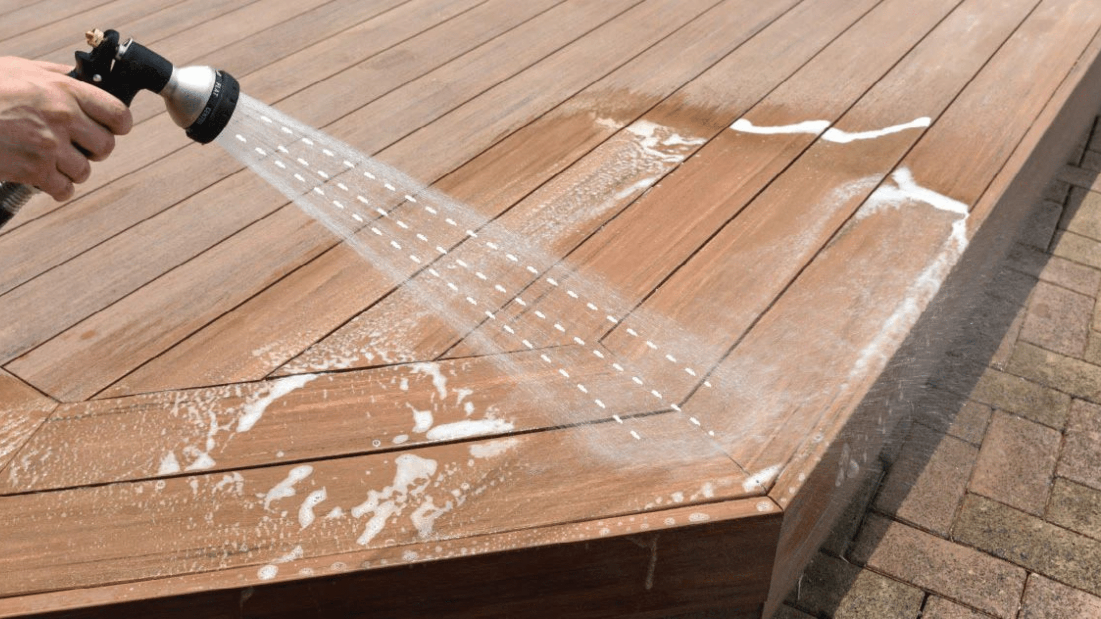 Rinsing a TimberTech deck with a garden hose to remove soap and dirt, demonstrating the gentle pressure washing technique used when cleaning TimberTech decking.